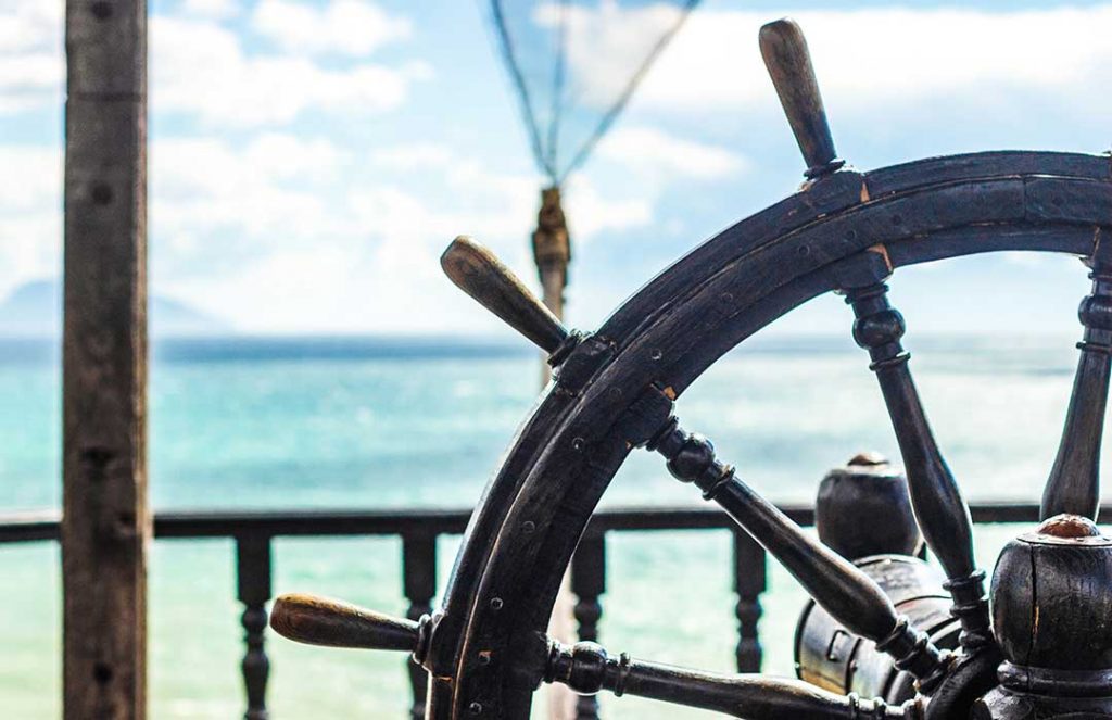 Nahaufnahme eines hölzernen Steuerrads mit Blick aufs Meer – Symbol für bewusste Führung und Navigation im Sozialwesen