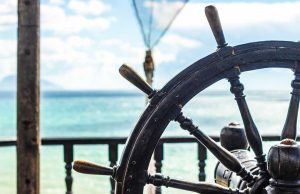 Nahaufnahme eines hölzernen Steuerrads mit Blick aufs Meer – Symbol für bewusste Führung und Navigation im Sozialwesen